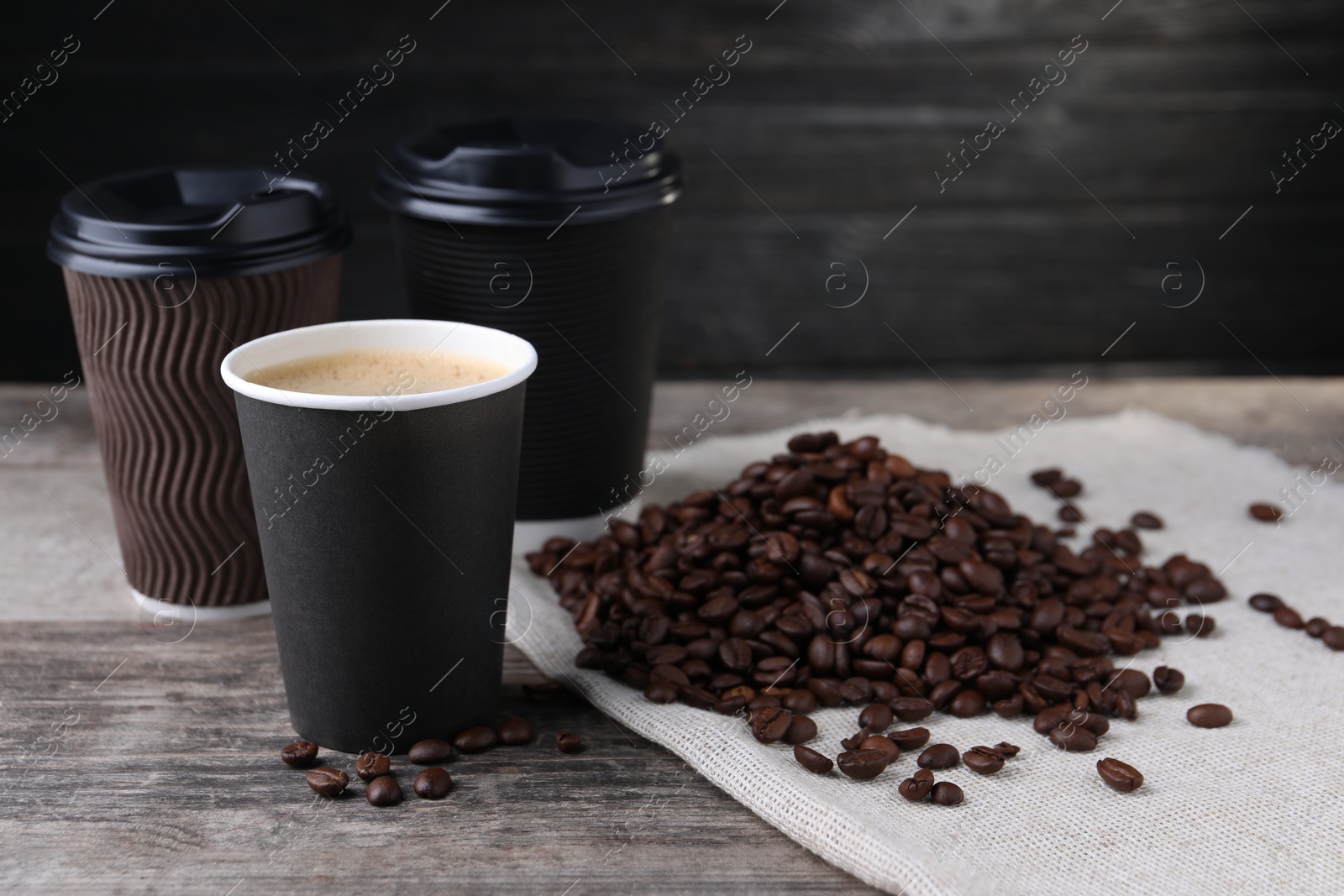 Photo of Coffee to go. Paper cups with tasty drink and roasted beans on wooden table, space for text