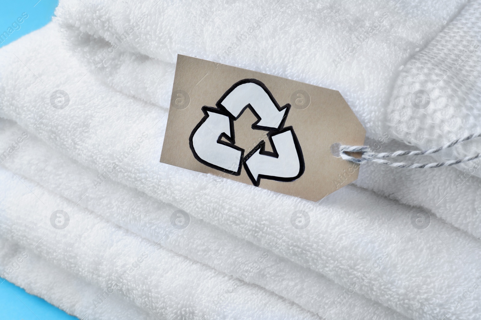 Photo of Stacked towels with recycling label on light blue background, closeup