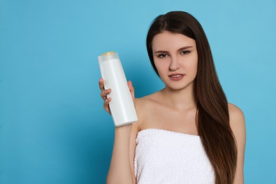 Photo of Beautiful young woman wrapped in towel holding bottle of shampoo on light blue background. Space for text