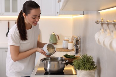 Photo of Smiling woman adding noodles into pot with soup in kitchen