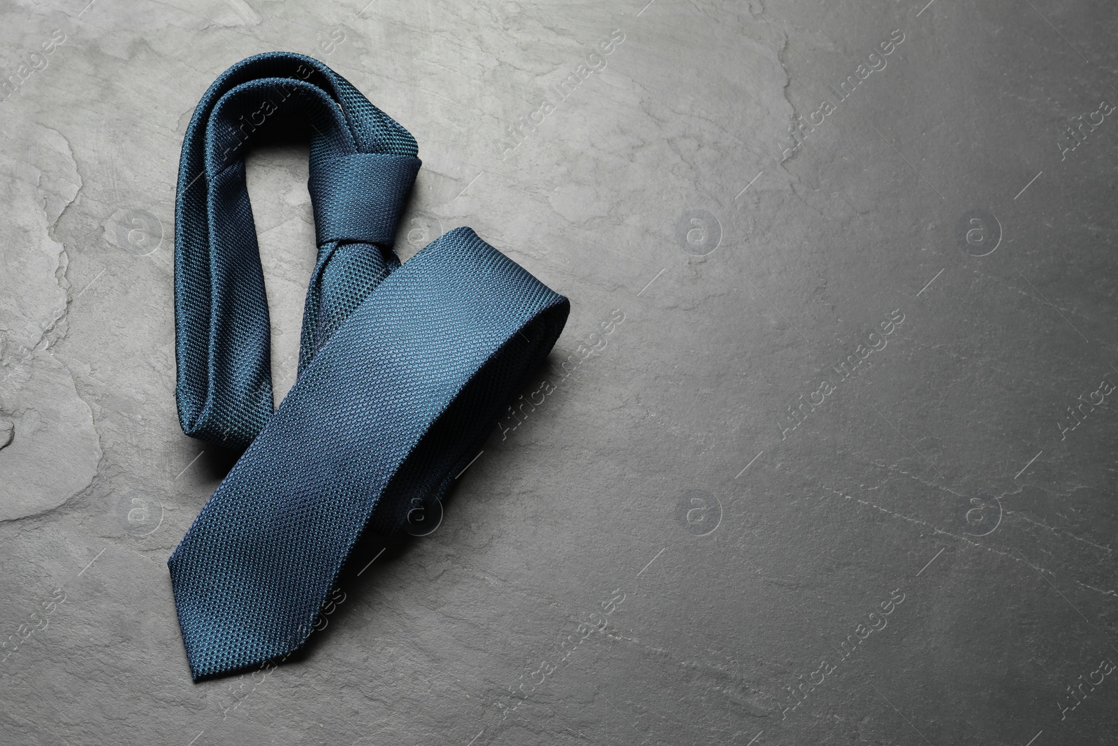 Photo of One blue necktie on grey textured table, top view. Space for text