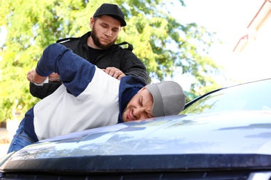 Police officer arresting criminal near car outdoors