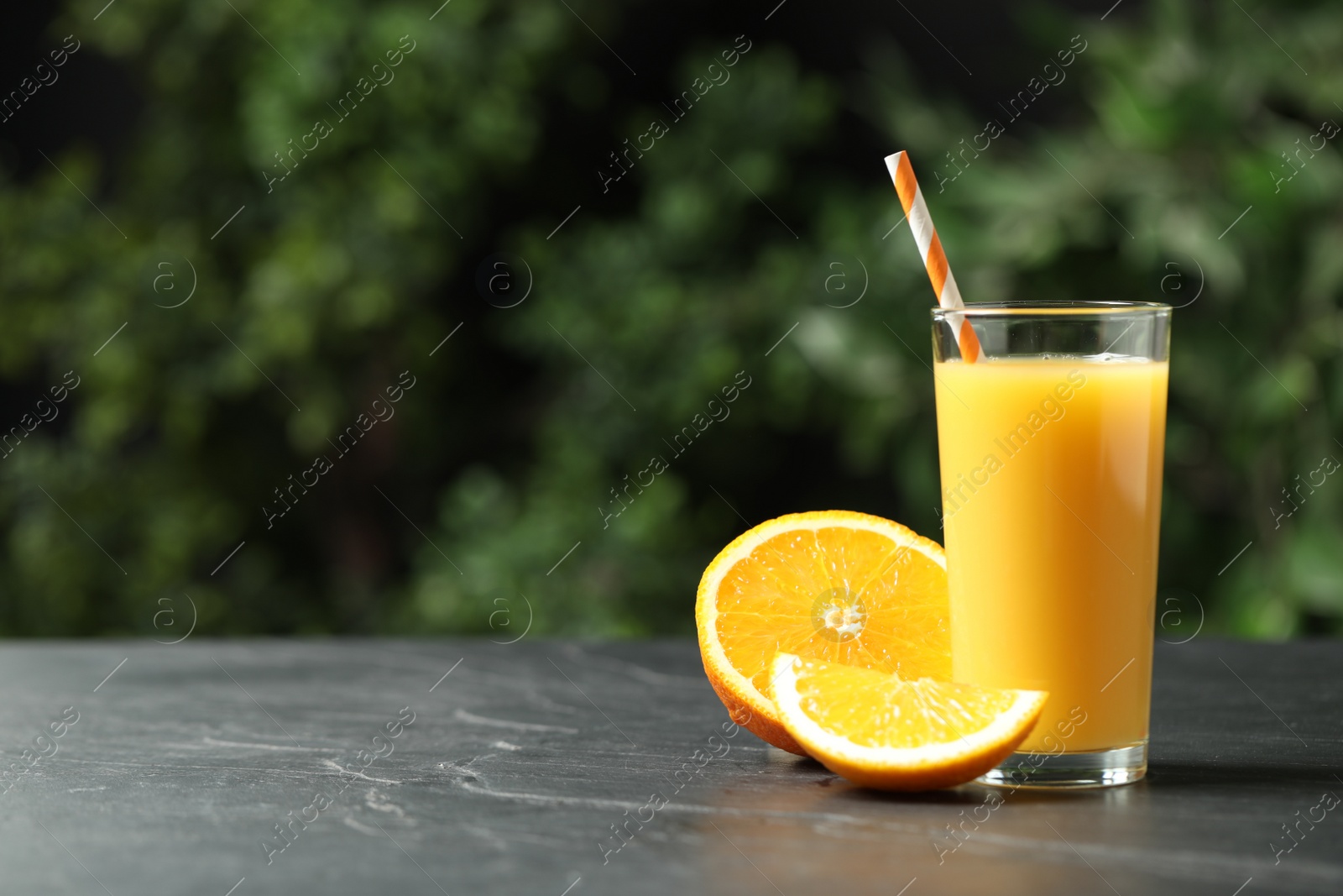 Photo of Glass of orange juice and fresh fruits on grey table. Space for text