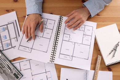 Photo of Man with sketchbook of construction drawings and pencil at wooden table, top view