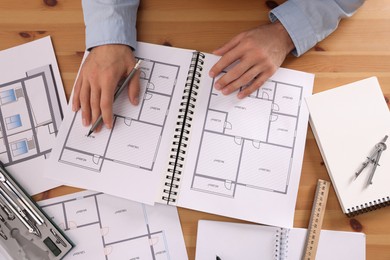 Man with sketchbook of construction drawings and pencil at wooden table, top view