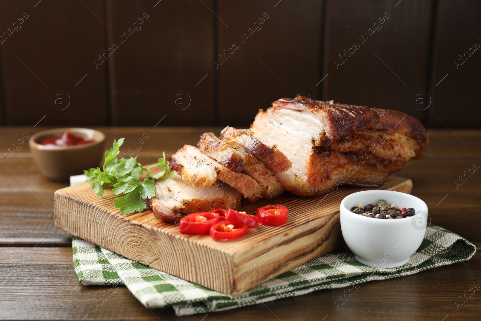 Photo of Pieces of baked pork belly served with sauce, chili pepper and parsley on wooden table