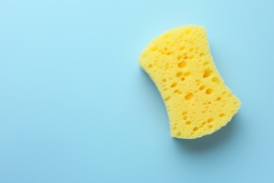 Photo of New yellow sponge on light blue background, top view. Space for text