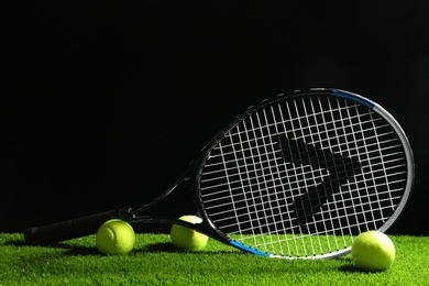 Tennis racket and balls on green grass against dark background. Sports equipment