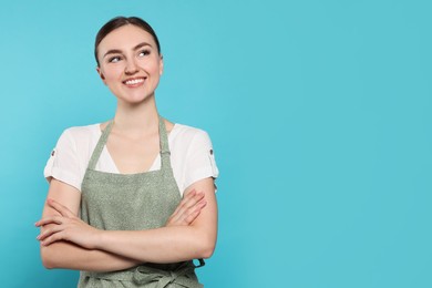 Beautiful young woman in clean apron with pattern on light blue background. Space for text