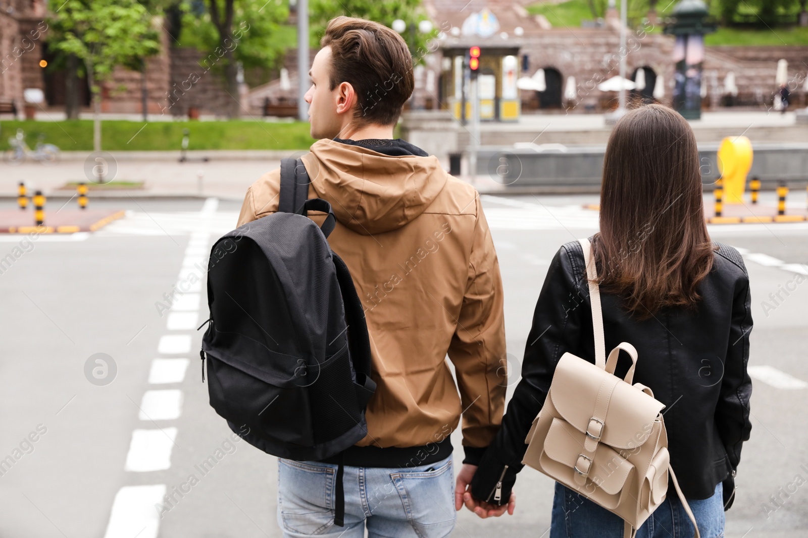 Photo of Young couple waiting to cross street, back view. Traffic rules and regulations