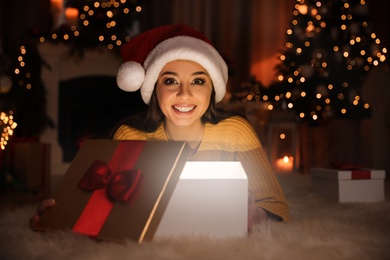 Young woman wearing Santa hat opening Christmas gift on floor at home