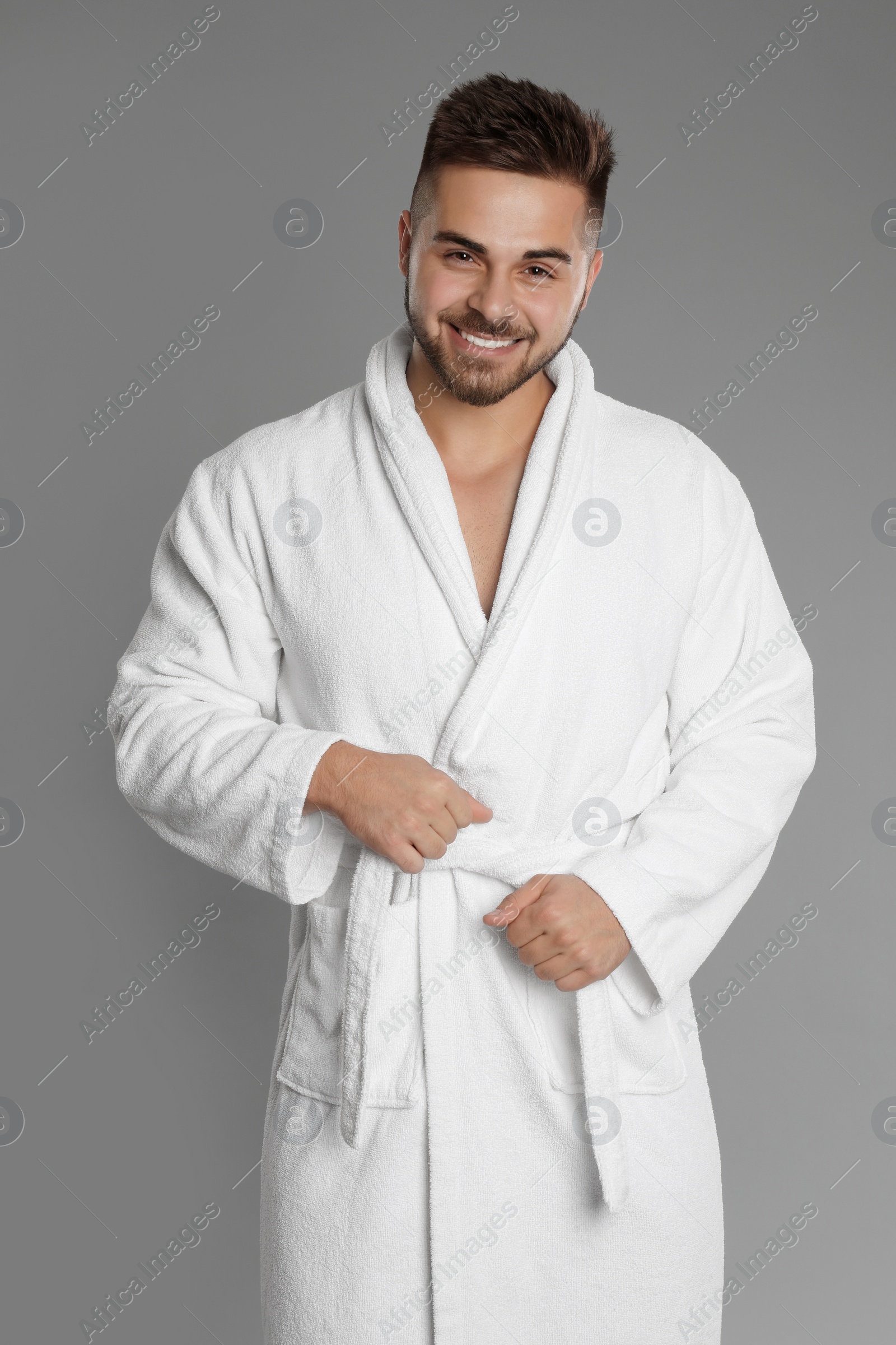 Photo of Happy young man in bathrobe on grey background