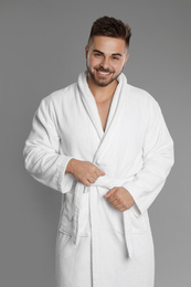 Happy young man in bathrobe on grey background