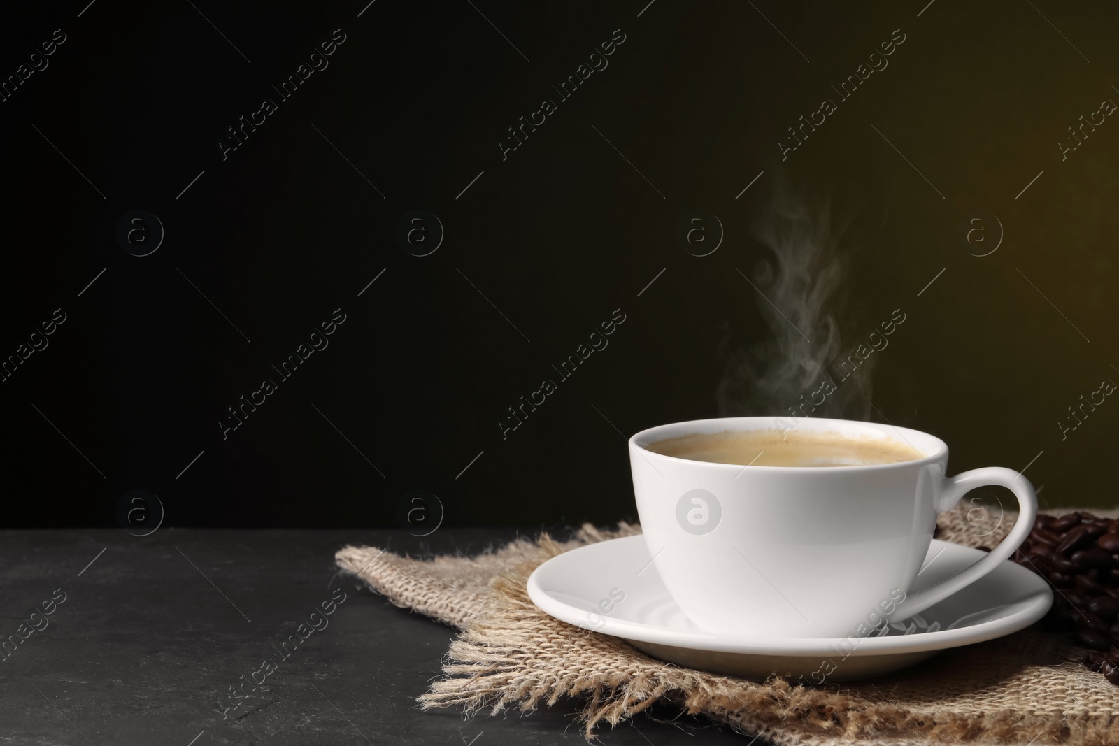 Image of Steaming coffee in cup and roasted beans on table. Space for text