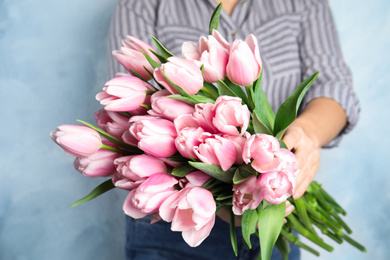 Woman with beautiful pink spring tulips on light blue background, closeup