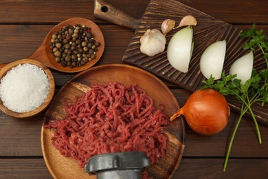 Photo of Meat grinder with beef mince, onion, parsley, garlic and spices on wooden table, flat lay