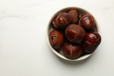 Roasted edible sweet chestnuts in bowl on white marble table, top view. Space for text