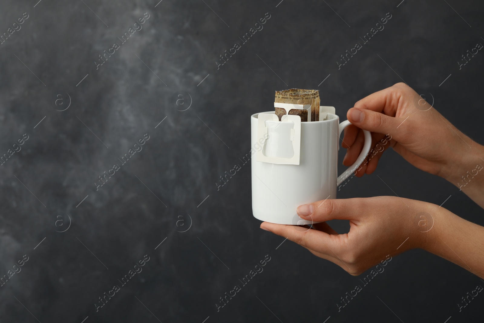 Photo of Woman holding cup with drip coffee bag on grey background, closeup. Space for text