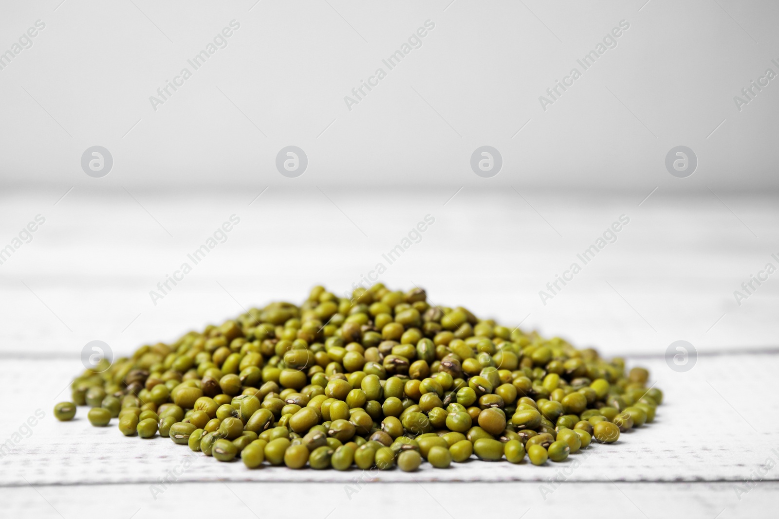 Photo of Pile of green mung beans on white wooden table, closeup. Space for text