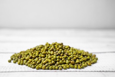 Photo of Pile of green mung beans on white wooden table, closeup. Space for text