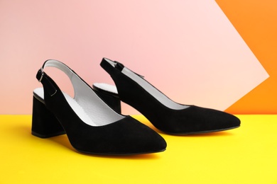Stylish female shoes on yellow table against color background