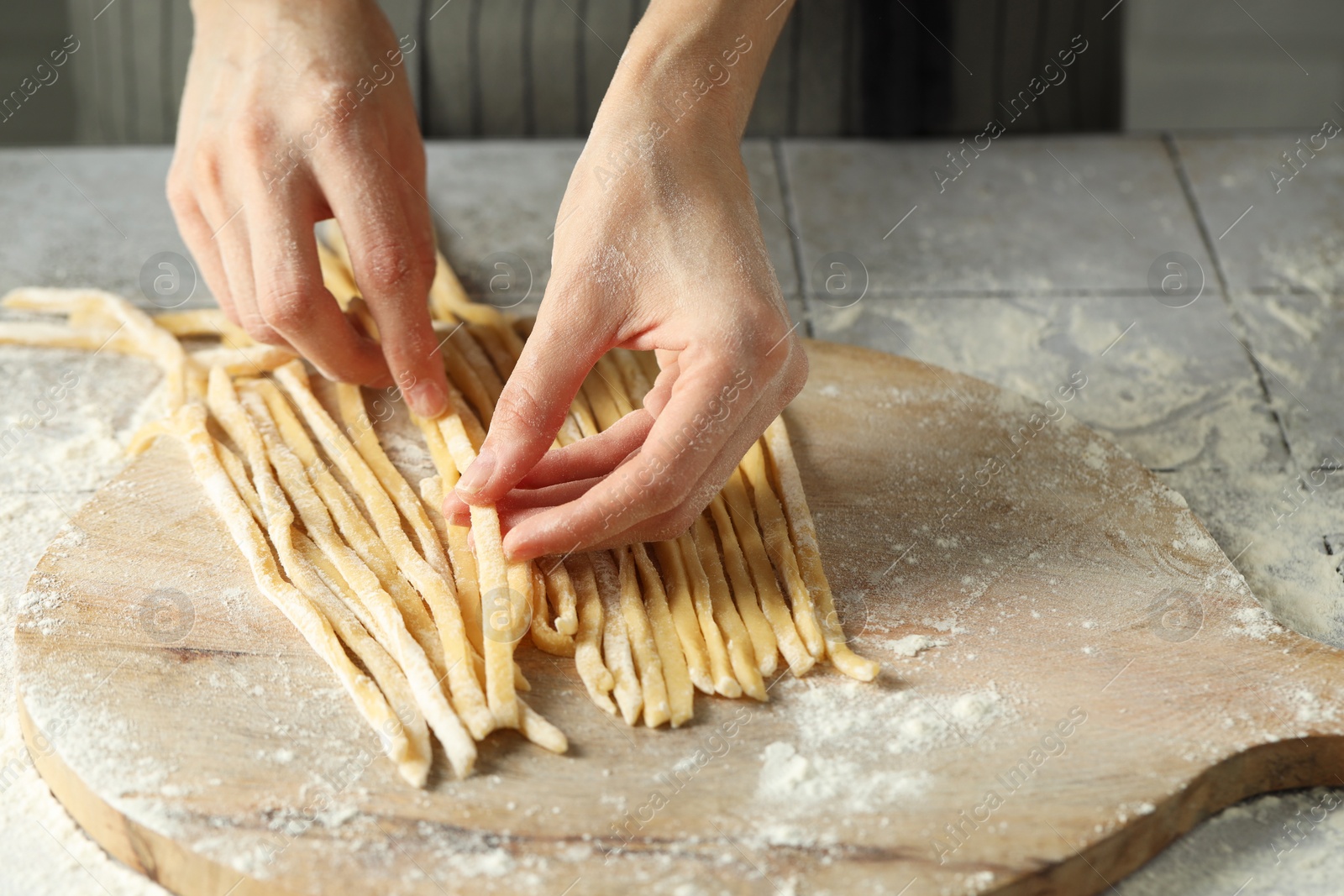 Photo of Woman with homemade pasta at light tiled table, closeup