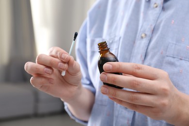 Woman holding bottle of brilliant green and cotton bud indoors, closeup