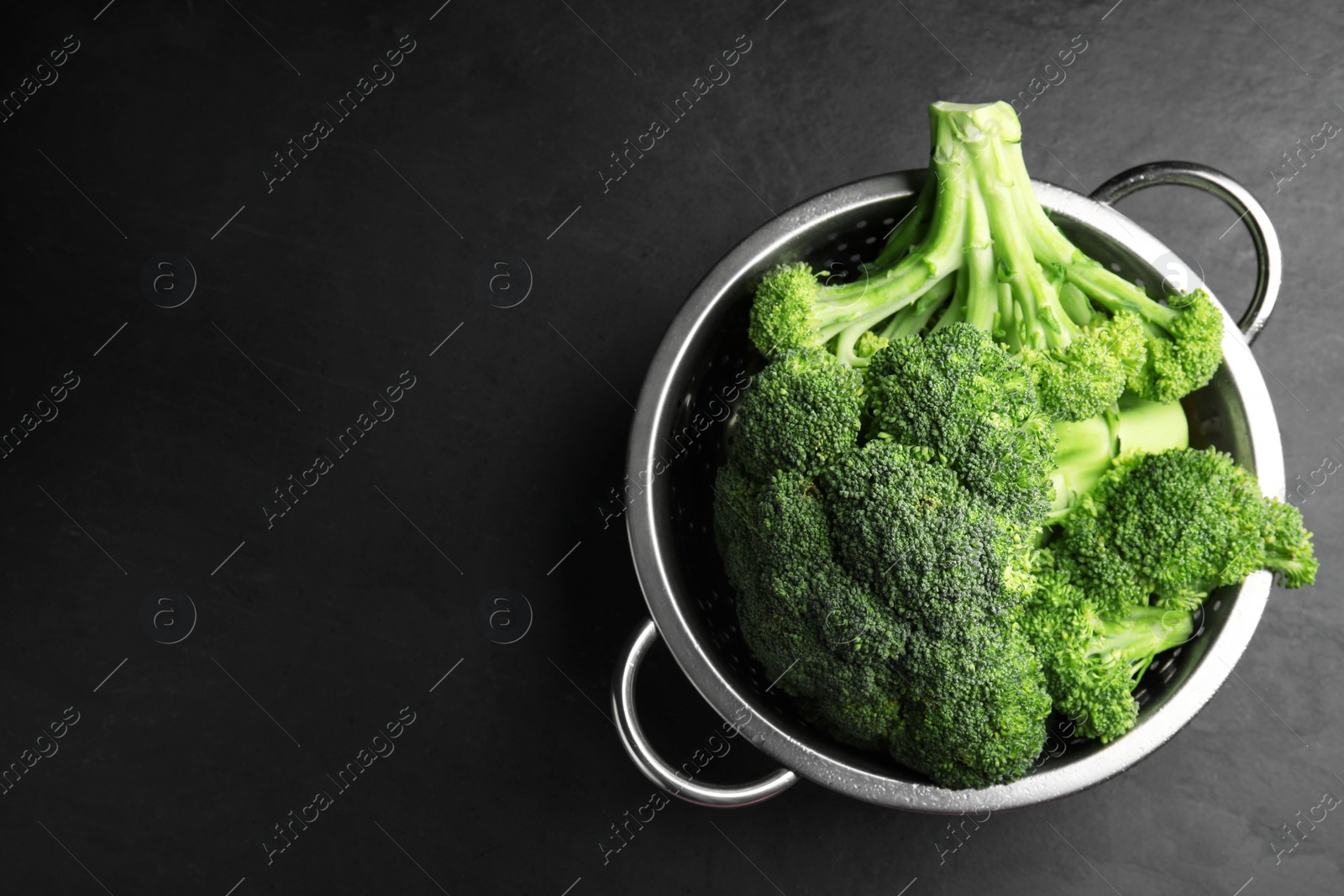 Photo of Fresh green broccoli in colander on black table, top view. Space for text