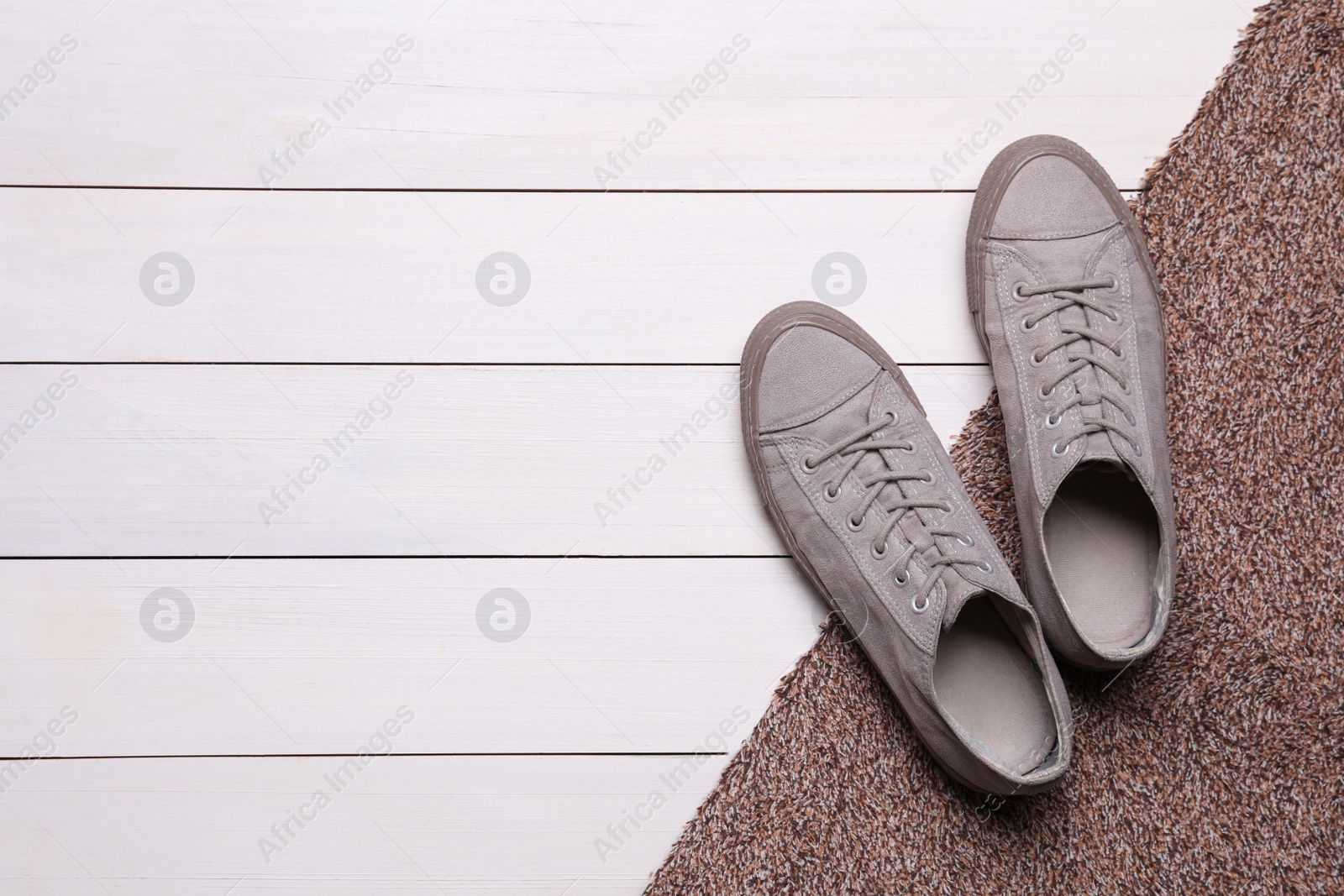 Photo of New clean door mat with shoes on white wooden floor, flat lay. Space for text