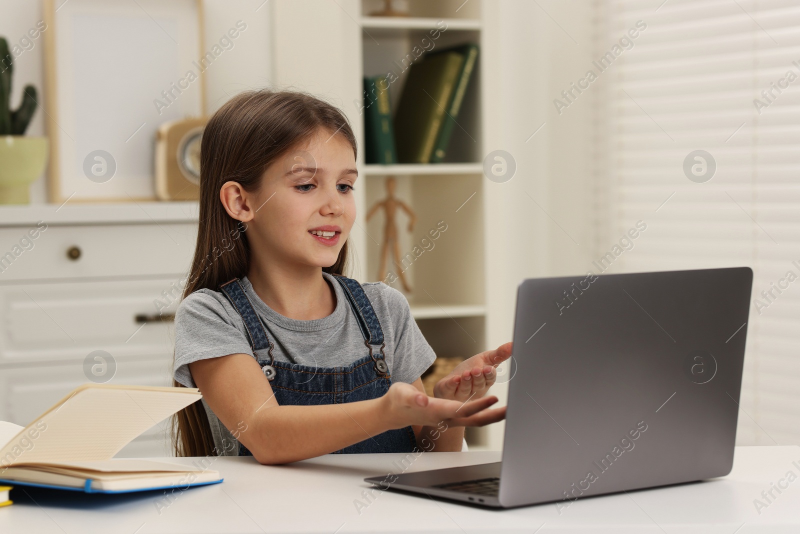 Photo of Cute girl having online lesson at white table indoors