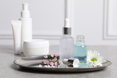 Bottles of cosmetic serum and beautiful flowers on gray table