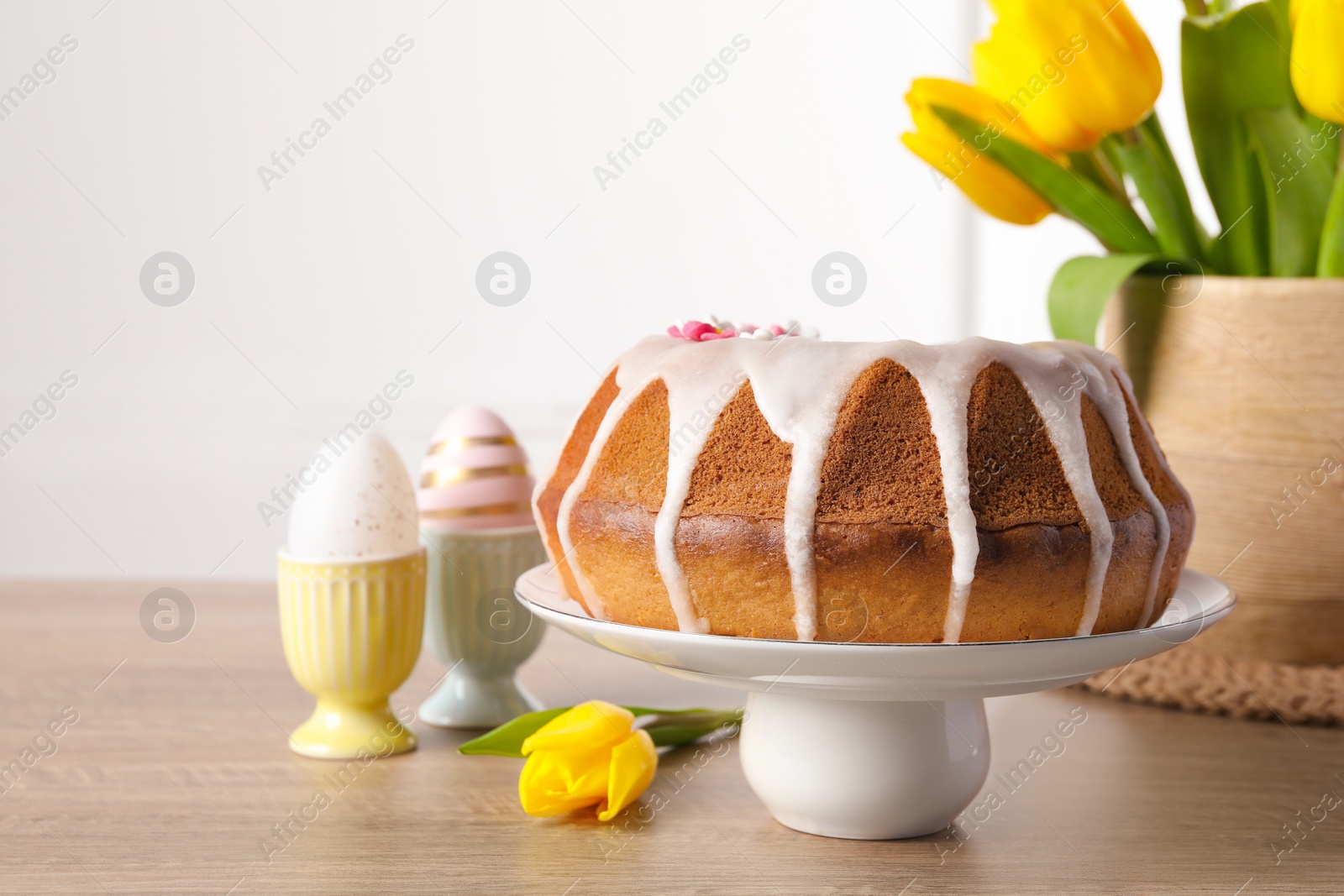 Photo of Delicious Easter cake decorated with sprinkles near beautiful tulips and painted eggs on wooden table. Space for text