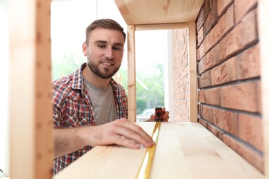 Photo of Young working man measuring wooden shelf indoors