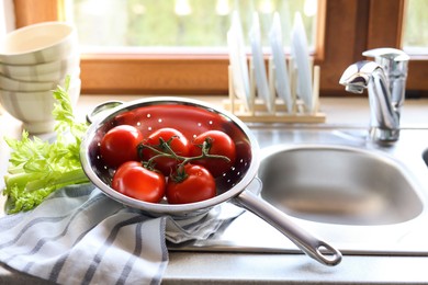 Photo of Colander with fresh raw tomatoes and celery near sink in kitchen