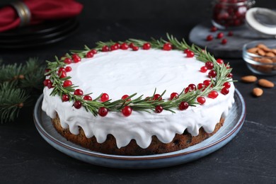 Traditional Christmas cake decorated with rosemary and cranberries on dark grey table, closeup