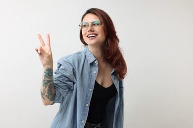 Photo of Beautiful tattooed woman showing V-sign on gray background