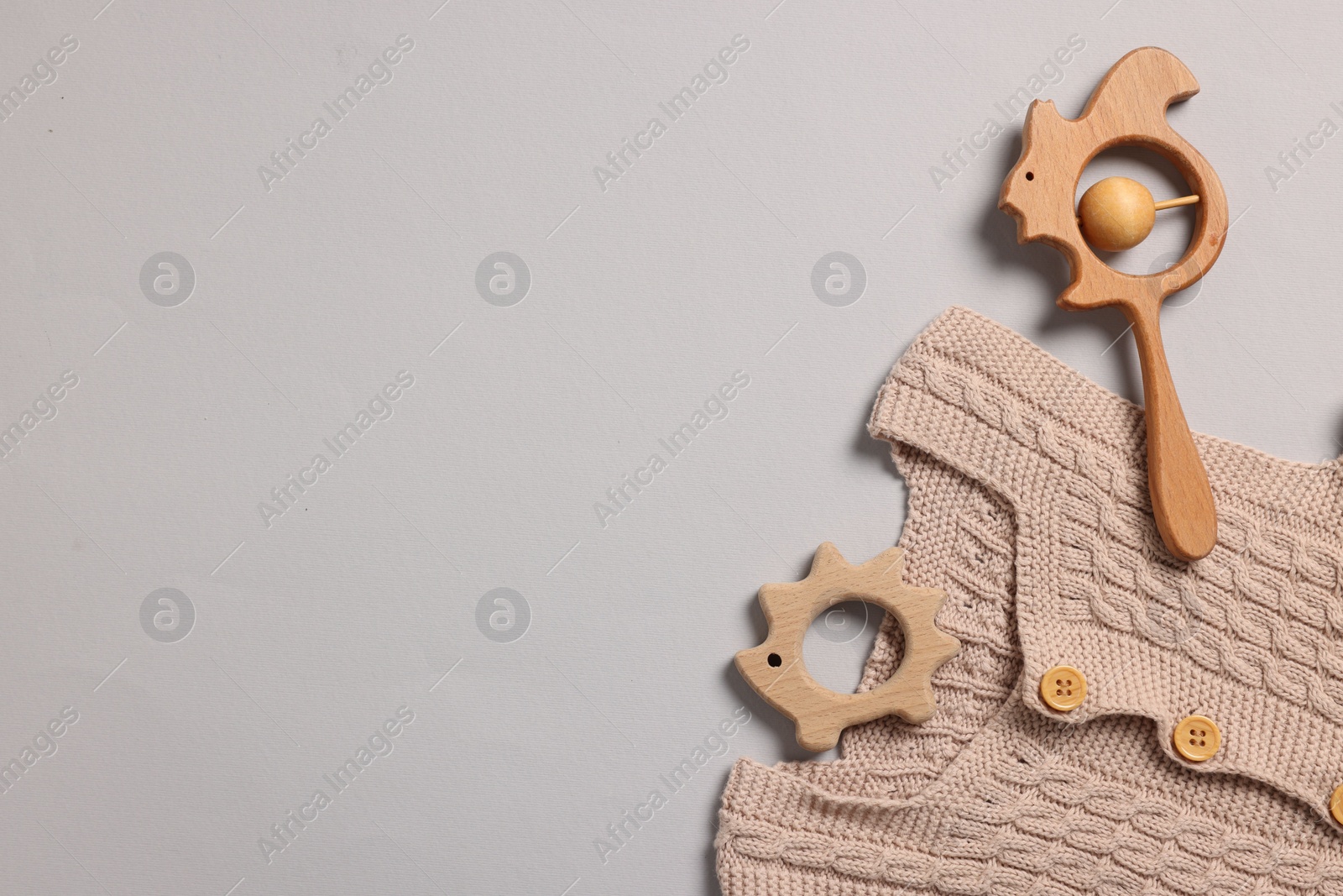 Photo of Baby accessories. Wooden rattle, teether and knitted cloth on grey background, top view. Space for text