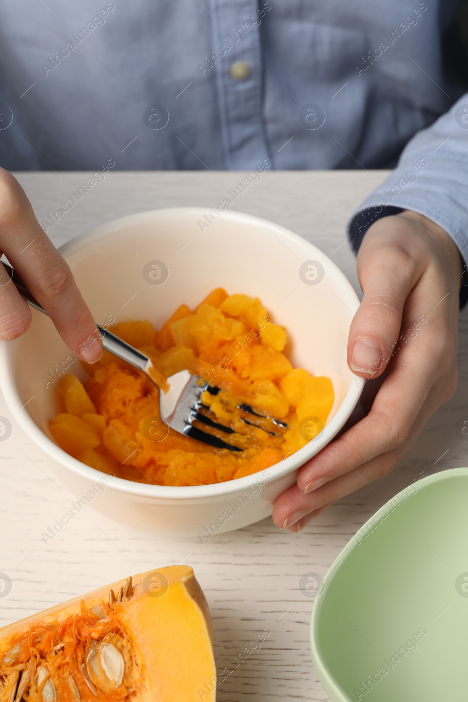 Photo of Woman making baby food with pumpkin at white wooden table, closeup