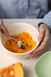 Woman making baby food with pumpkin at white wooden table, closeup
