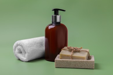 Photo of Soap bars, bottle dispenser and towel on green background