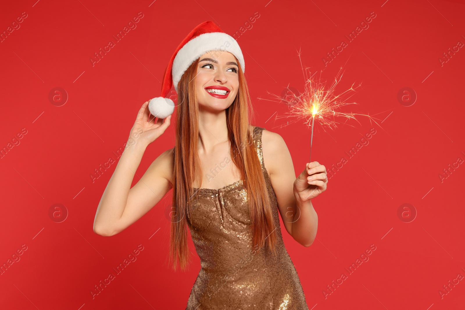 Photo of Young woman in Santa hat with burning sparkler on red background. Christmas celebration