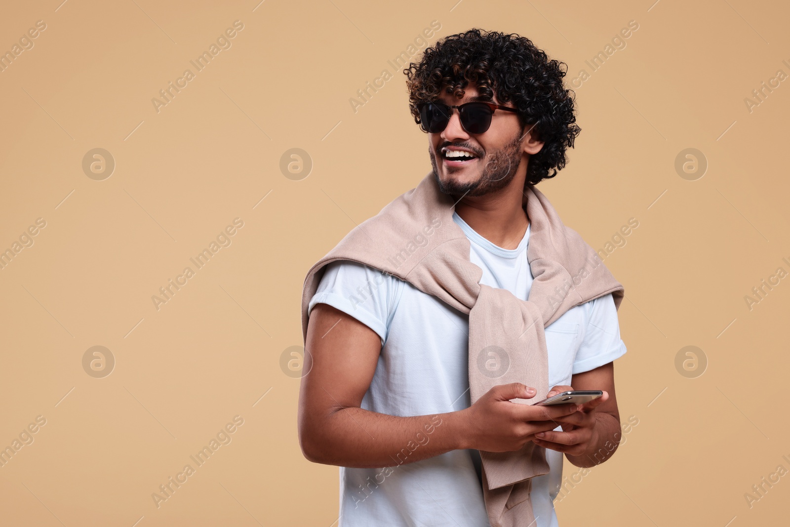 Photo of Handsome young smiling man in sunglasses on beige background. Space for text