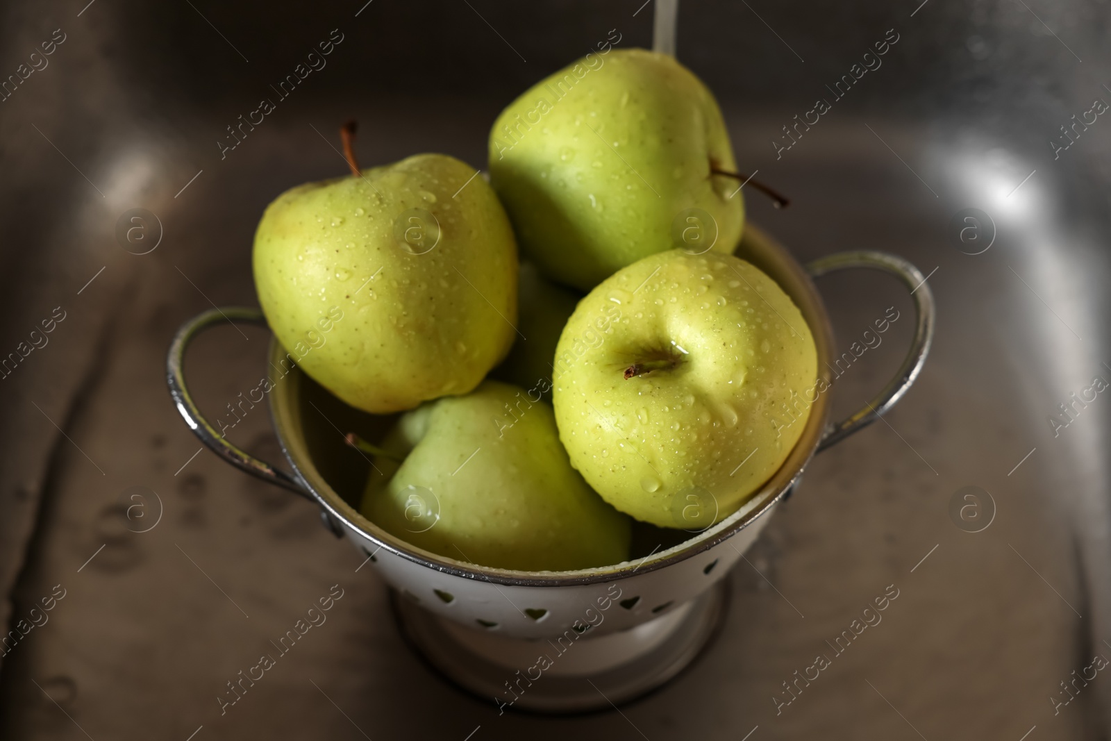 Photo of Washing fresh apples with tap water in metal colander inside sink