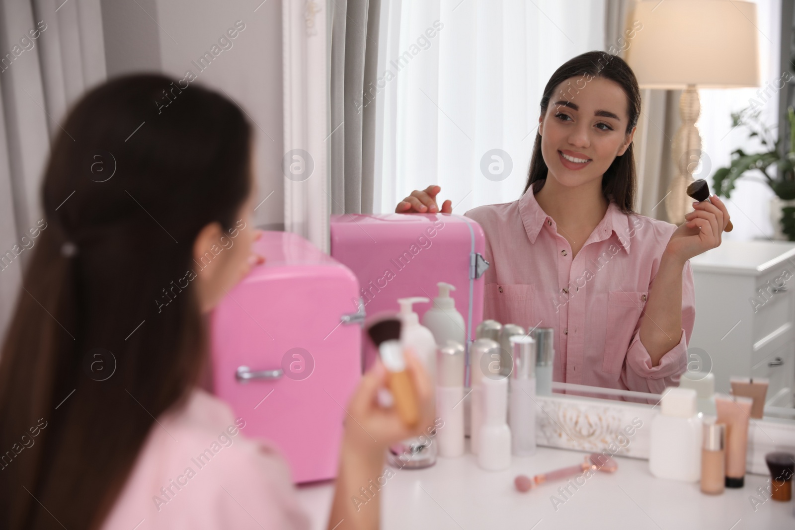 Photo of Woman getting ready at dressing table with cosmetic fridge indoors