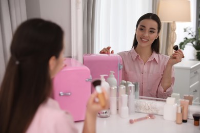 Photo of Woman getting ready at dressing table with cosmetic fridge indoors