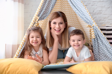 Photo of Nanny and little children reading book in tent at home