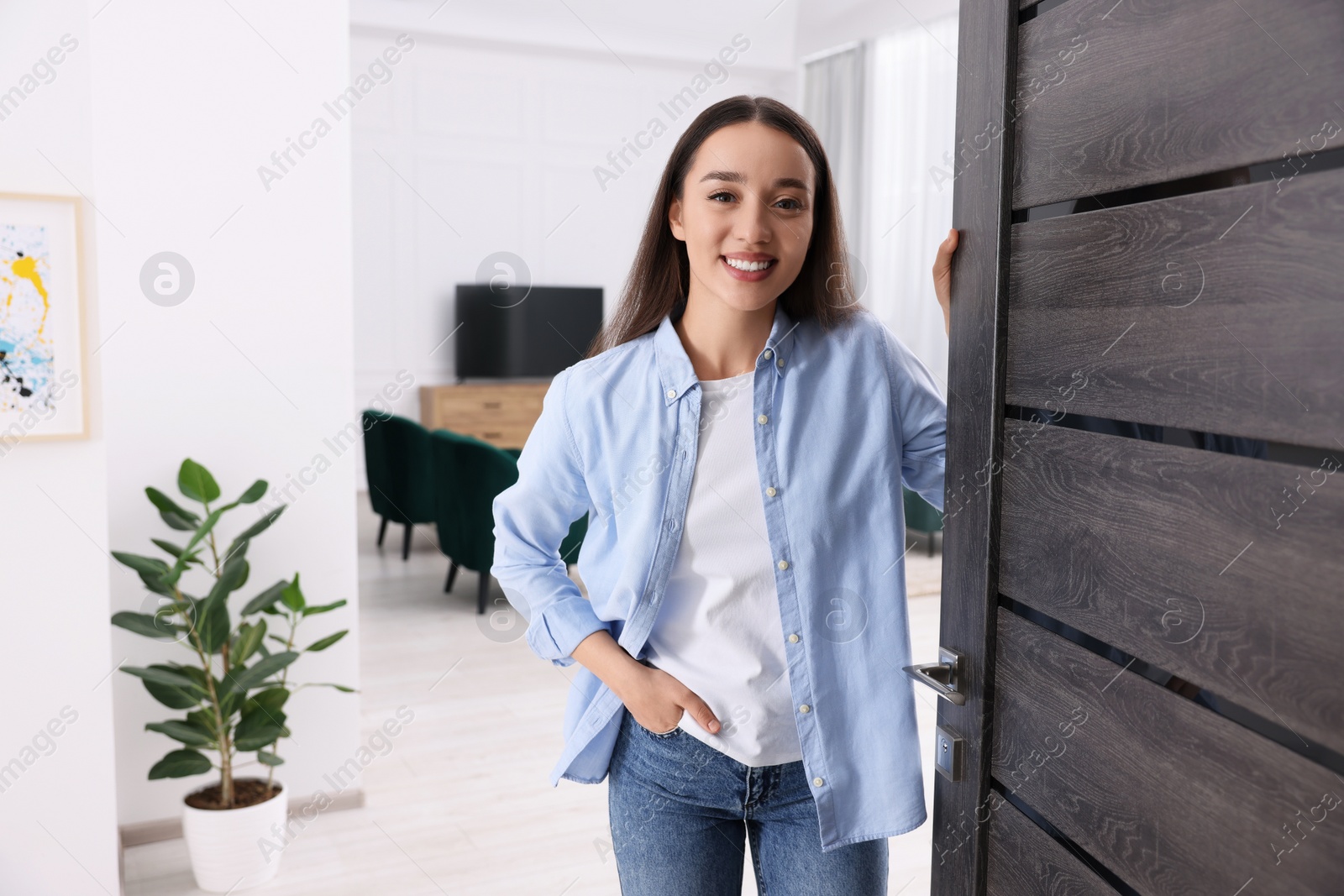 Photo of Happy woman standing near door, space for text. Invitation to come indoors