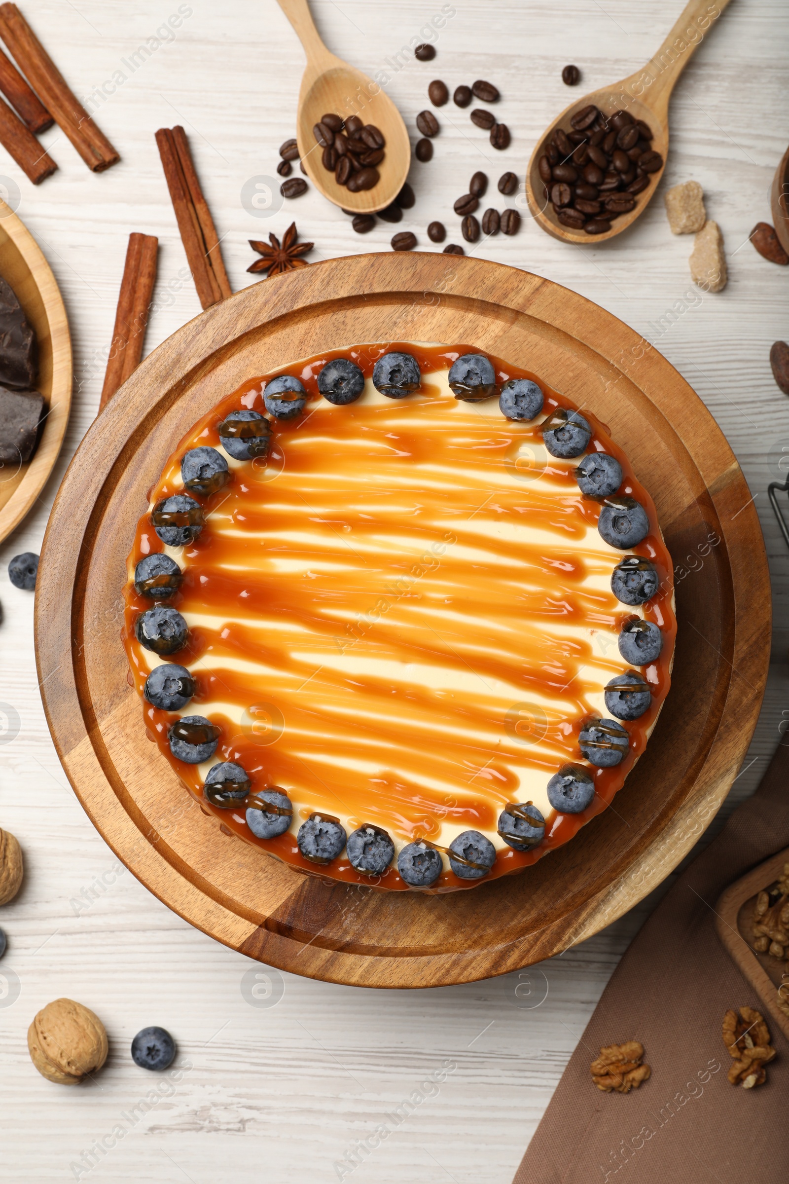 Photo of Delicious cheesecake with caramel and blueberries on white wooden table, flat lay