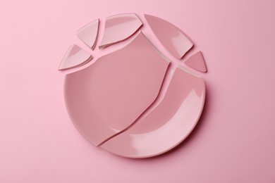 Photo of Pieces of broken ceramic plate on pink background, flat lay