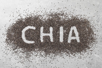 Word CHIA written in pile of seeds on grey table, top view